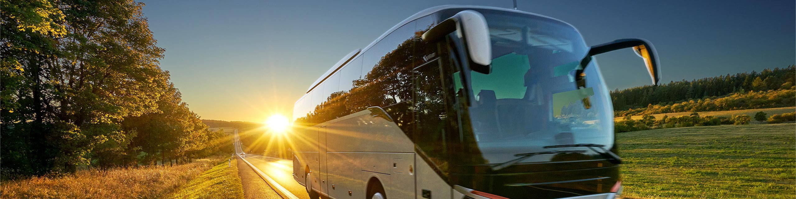 Reisebus fährt auf Landstraße mit Sonne im Hintergrund