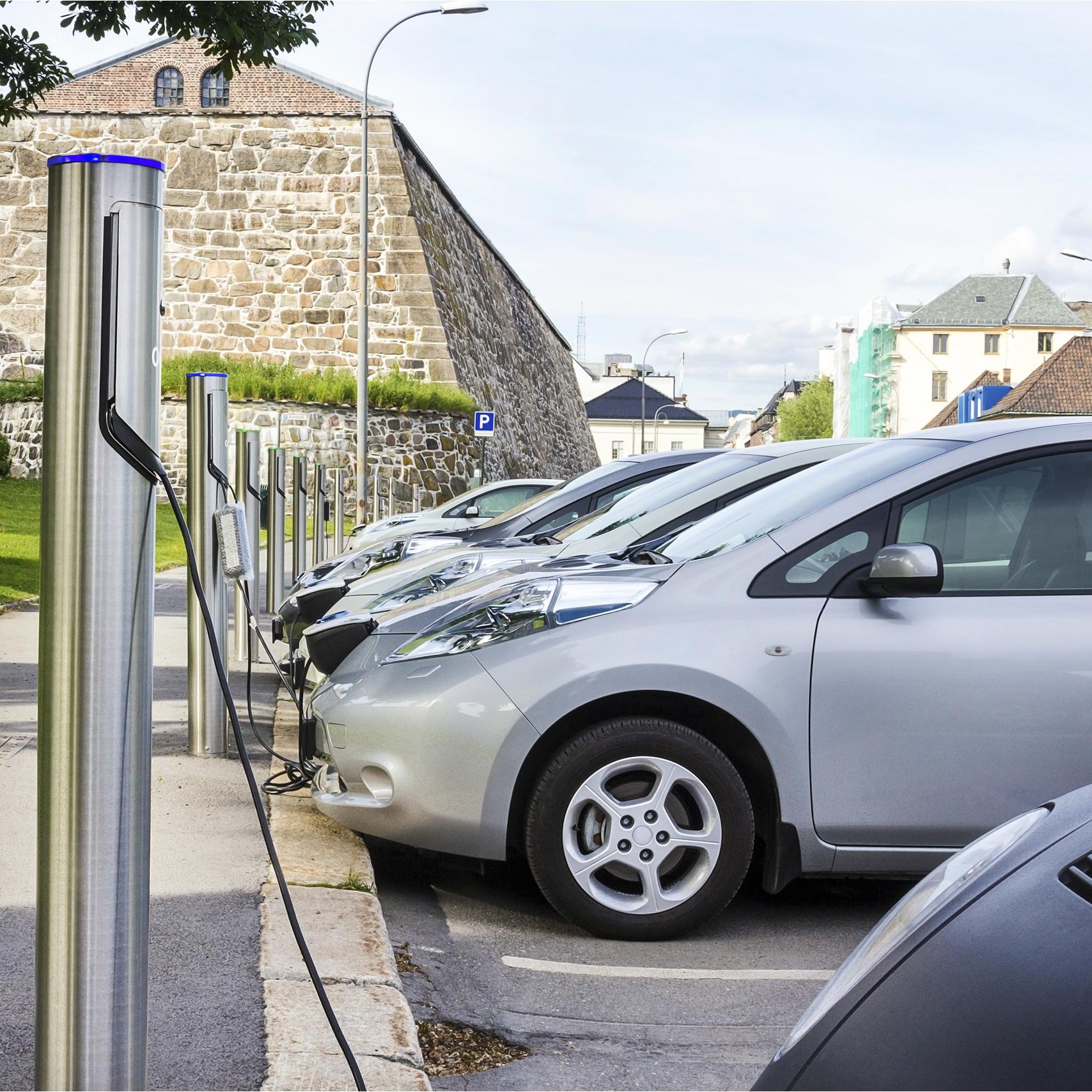 E-Autos laden Strom an Ladestationen vor einer Stadtmauer E-Autos laden Strom an Ladestationen vor einer Stadtmauer