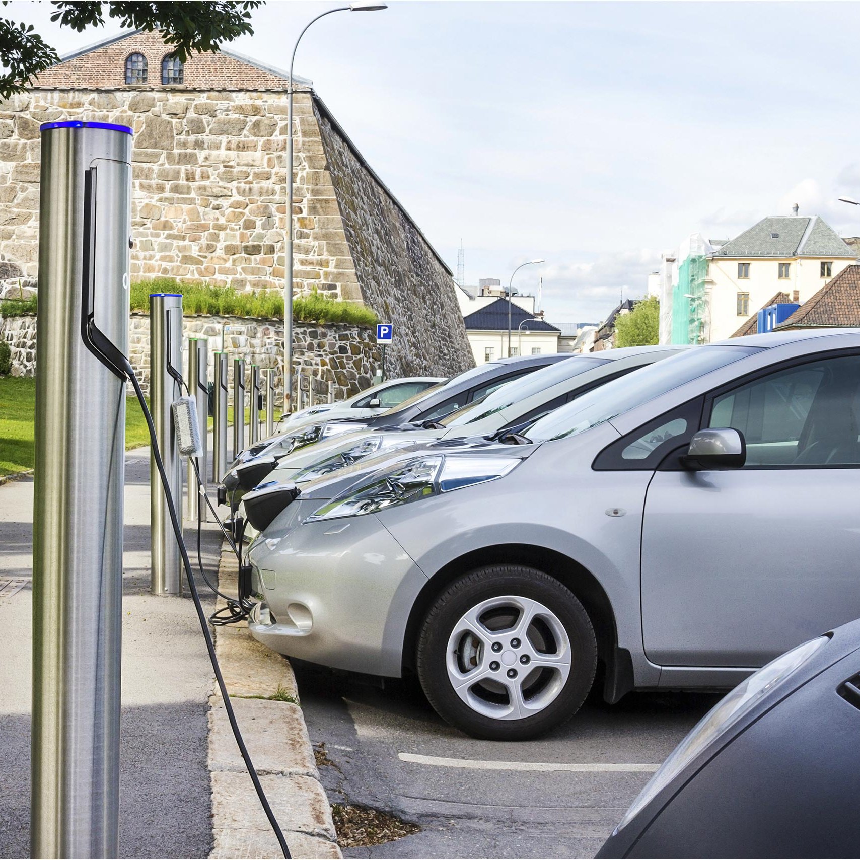 E-Autos laden Strom an Ladestationen vor einer Stadtmauer E-Autos laden Strom an Ladestationen vor einer Stadtmauer