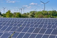 Freiflächen-Solaranlage mit Windenergieanlagen und Bäumen im Hintergrund