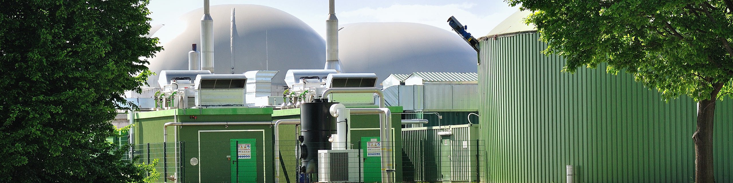 Biogasanlage mit Bäumen und Wiese im Vordergrund