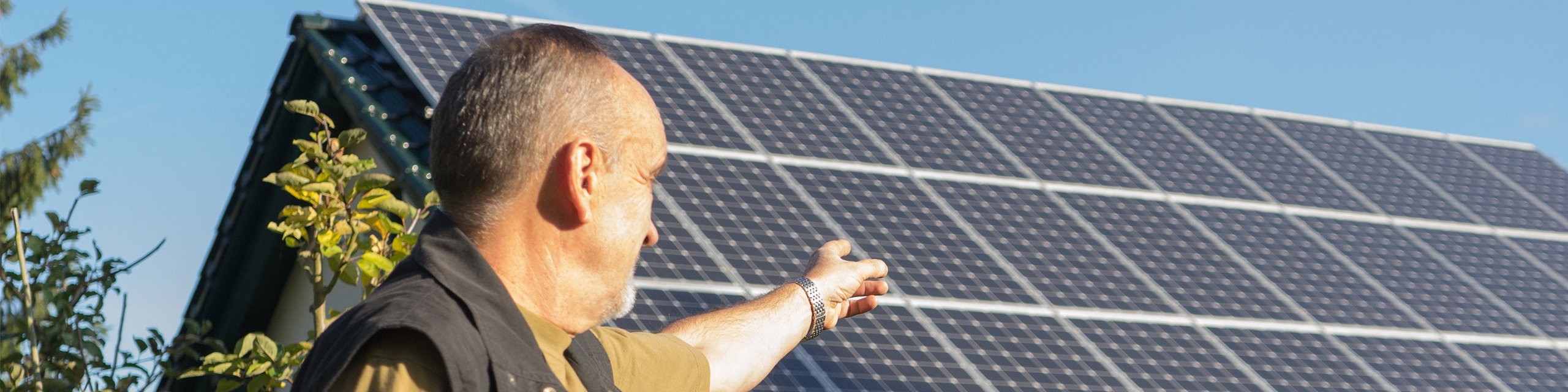 Hauseigentümer mit Solaranlage Hauseigentümer steht vor seinem Einfamilienhaus und zeigt auf die Dachsolaranlage.