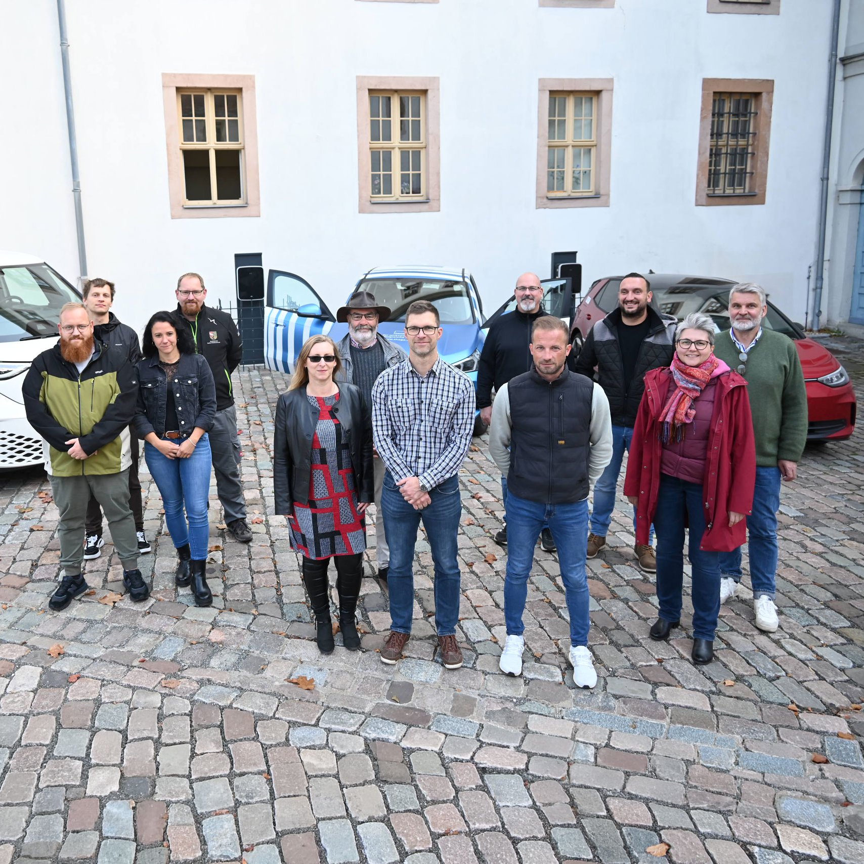 Eine Gruppe von E-Lotsen aus dem Saale-Holzlandkreis steht vor drei Elektroautos.