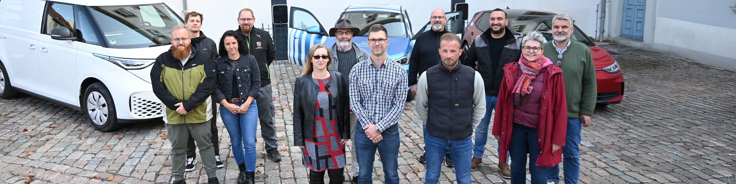 E-Lotsen Gruppenbild Eine Gruppe von E-Lotsen aus dem Saale-Holzlandkreis steht vor drei Elektroautos.