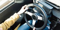 Ein E-Auto von oben fotografiert, man sieht das Lenkrad und zwei Arme einer Frau während der Fahrt. 