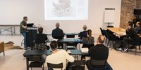 kleine Gruppe von ca. 9 Personen verfolgt gespannt eine Präsentation. Szene wurde von hinten fotografiert