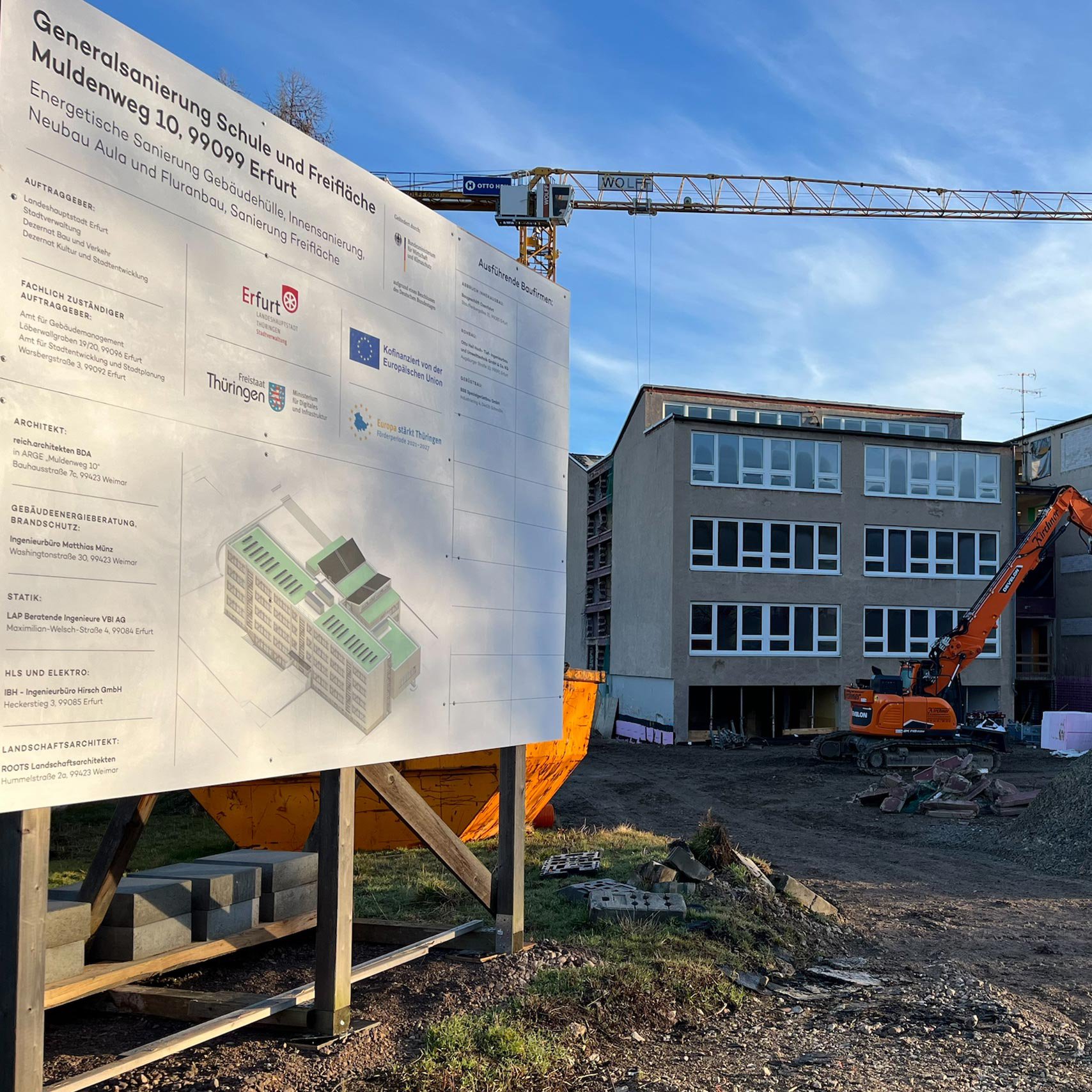 Schulgebäude mit Bagger und Baustellenplakat