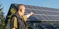 Hauseigentümer steht vor seinem Einfamilienhaus und zeigt auf die Dachsolaranlage.