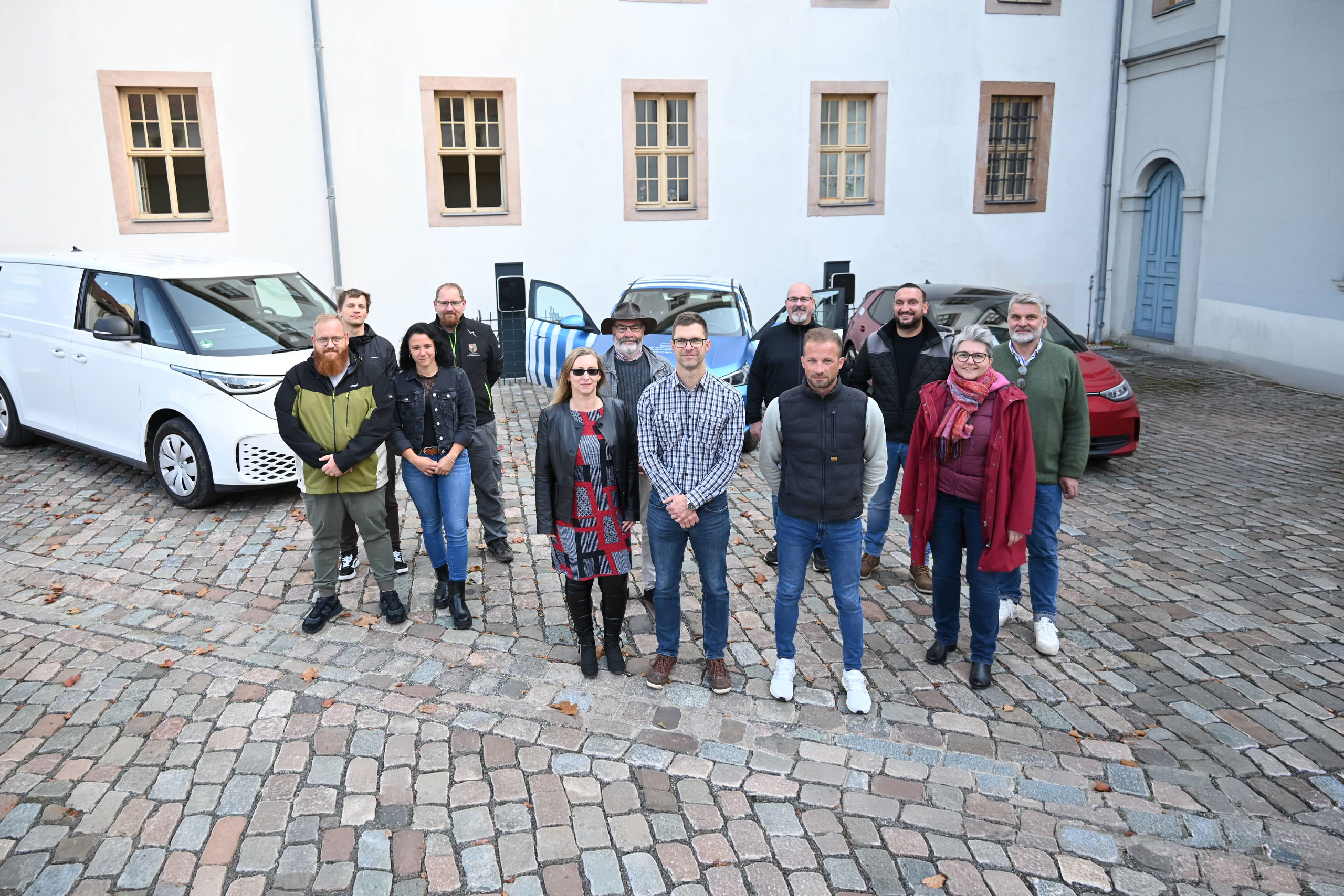 E-Lotsen Gruppenbild Eine Gruppe von E-Lotsen aus dem Saale-Holzlandkreis steht vor drei Elektroautos.