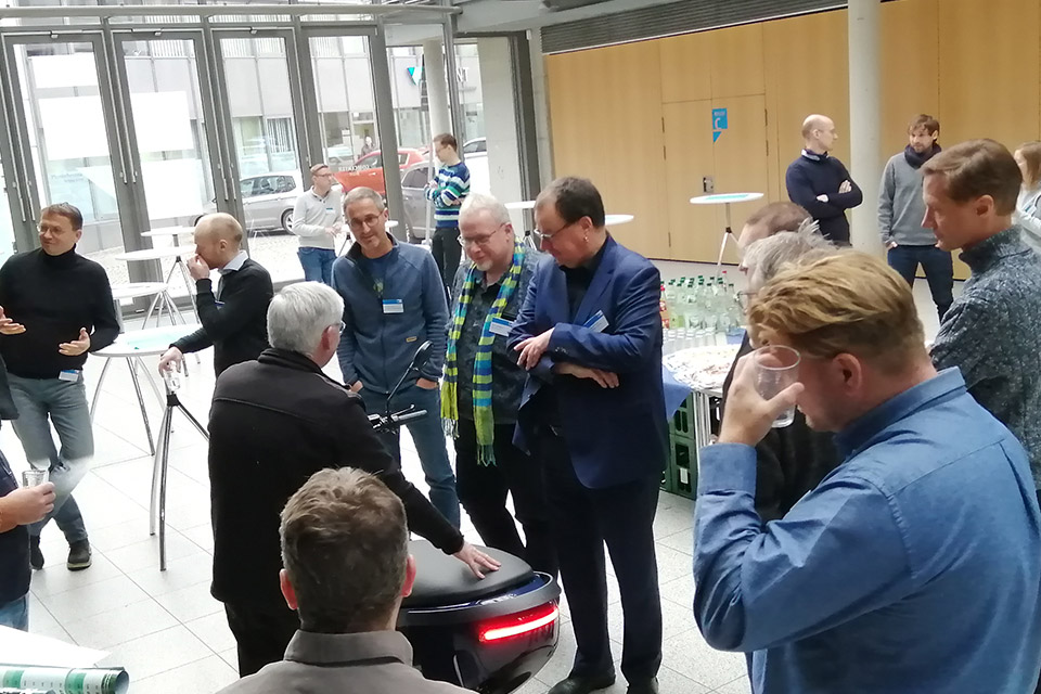 Mehrere Thüringer E-Lotsen stehen während einer Tagungspause um einen E-Roller