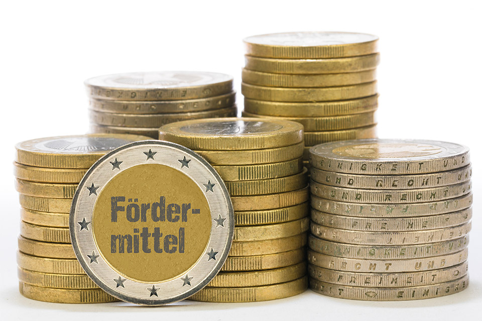 Gestapelte Euro-Münzen, auf denen Fördermittel steht statt Zahlen