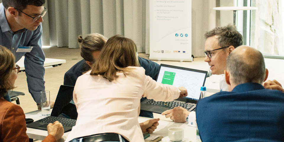 Workshop Gruppengespräch Sechs Personen sitzen um einen Laptop und eine Frau zeigt mit ihrem Finger auf den Bildschirm.