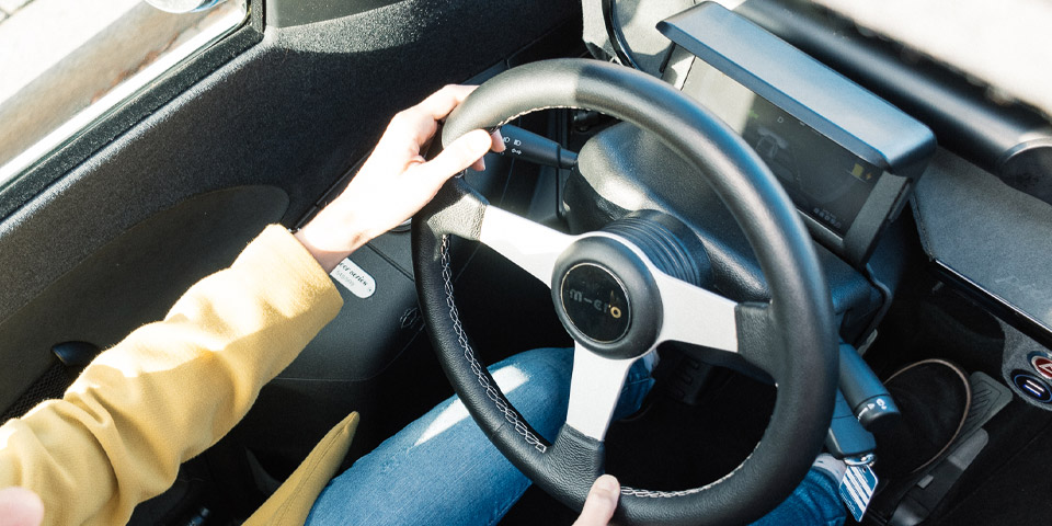 Ein E-Auto von oben fotografiert, man sieht das Lenkrad und zwei Arme einer Frau während der Fahrt. 